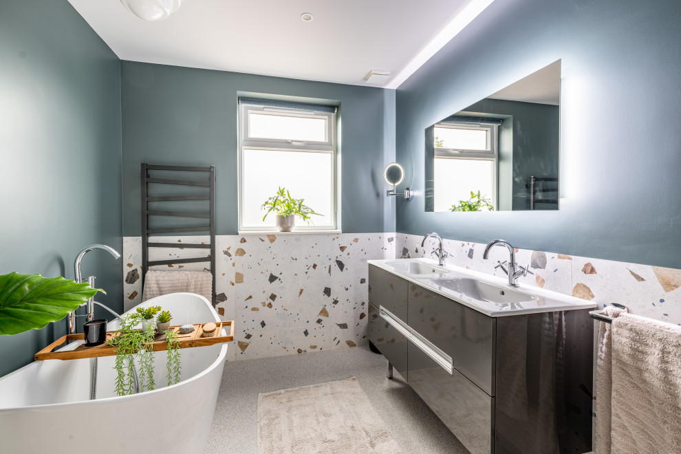 На фото: большая главная ванная комната в современном стиле с серыми фасадами, отдельно стоящей ванной, монолитной раковиной, плоскими фасадами, синими стенами, серым полом, белой столешницей, тумбой под две раковины и напольной тумбой с