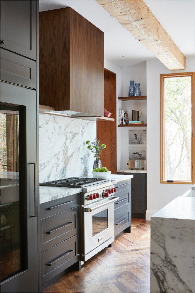Small single-wall open plan kitchen in Toronto with a farmhouse sink, shaker cabinets, black cabinets, marble benchtops, multi-coloured splashback, marble splashback, medium hardwood floors, with island, brown floor, multi-coloured benchtop and exposed beam.