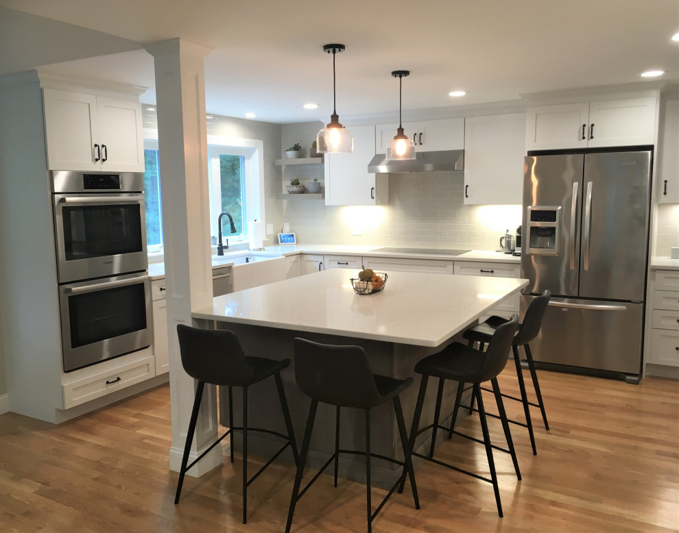Example of a large transitional u-shaped light wood floor and brown floor eat-in kitchen design in Boston with a farmhouse sink, shaker cabinets, white cabinets, quartz countertops, beige backsplash, subway tile backsplash, stainless steel appliances, an island and white countertops