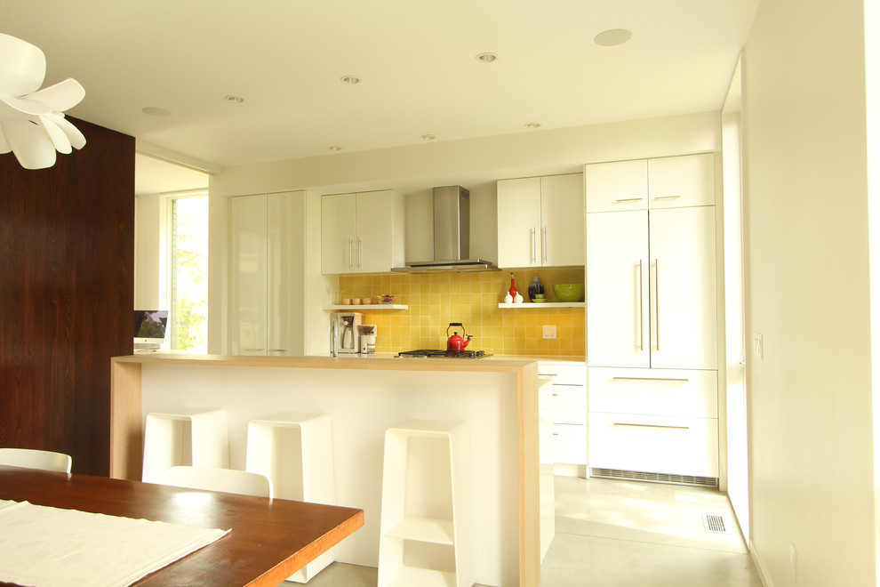 This is an example of a small modern single-wall open plan kitchen in Other with a double-bowl sink, flat-panel cabinets, white cabinets, quartz benchtops, yellow splashback, ceramic splashback, panelled appliances, concrete floors and with island.