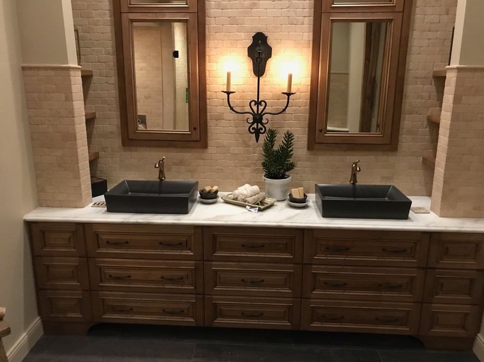 Design ideas for a mid-sized mediterranean master bathroom in Phoenix with raised-panel cabinets, dark wood cabinets, a freestanding tub, an alcove shower, a one-piece toilet, beige tile, stone tile, beige walls, dark hardwood floors, a vessel sink, marble benchtops, brown floor and a hinged shower door.