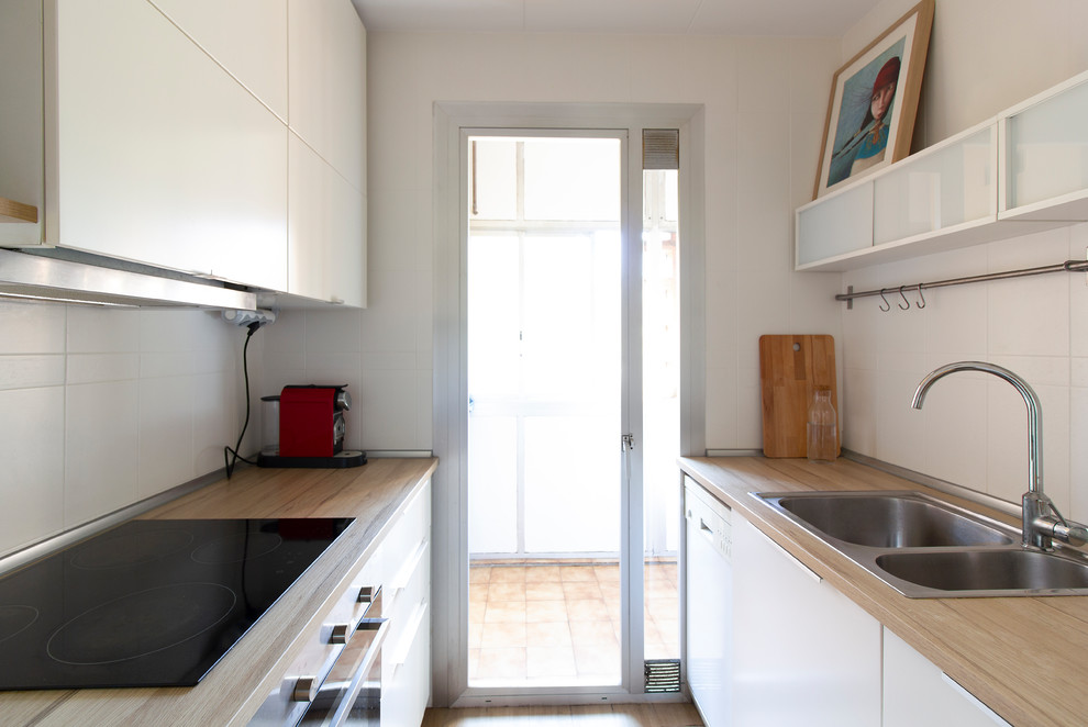 Small scandinavian galley separate kitchen in Barcelona with a double-bowl sink, flat-panel cabinets, white cabinets, laminate benchtops, white splashback, ceramic splashback, stainless steel appliances, linoleum floors and brown floor.