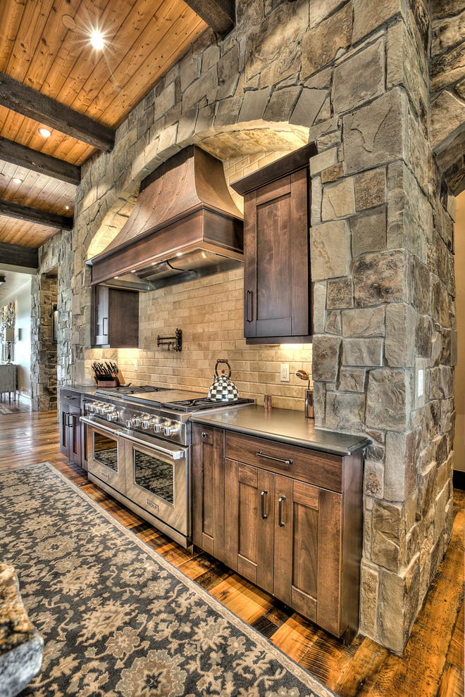 This is an example of an expansive country l-shaped eat-in kitchen in Denver with an undermount sink, shaker cabinets, medium wood cabinets, granite benchtops, beige splashback, stone tile splashback, stainless steel appliances, medium hardwood floors and multiple islands.