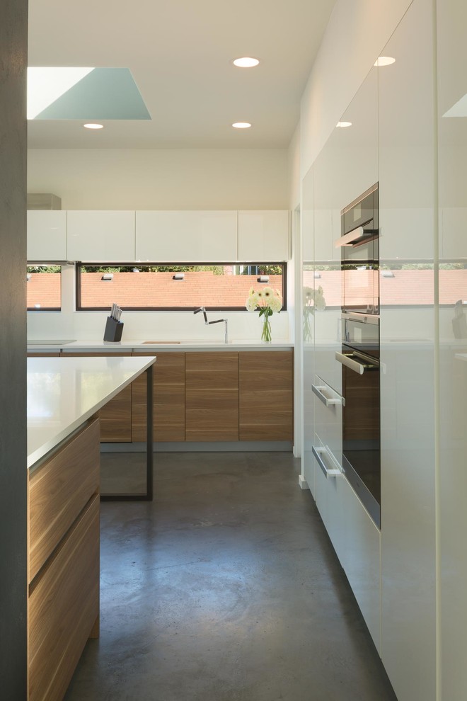 Example of a mid-sized minimalist l-shaped concrete floor open concept kitchen design in Seattle with an undermount sink, flat-panel cabinets, medium tone wood cabinets, quartz countertops, white backsplash, glass sheet backsplash, black appliances and an island