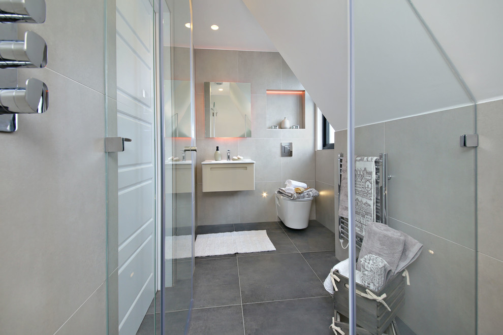 Photo of a mid-sized modern master bathroom in London with flat-panel cabinets, beige cabinets, an open shower, a wall-mount toilet, gray tile, porcelain tile, grey walls, porcelain floors, a wall-mount sink, solid surface benchtops, grey floor, a hinged shower door and white benchtops.
