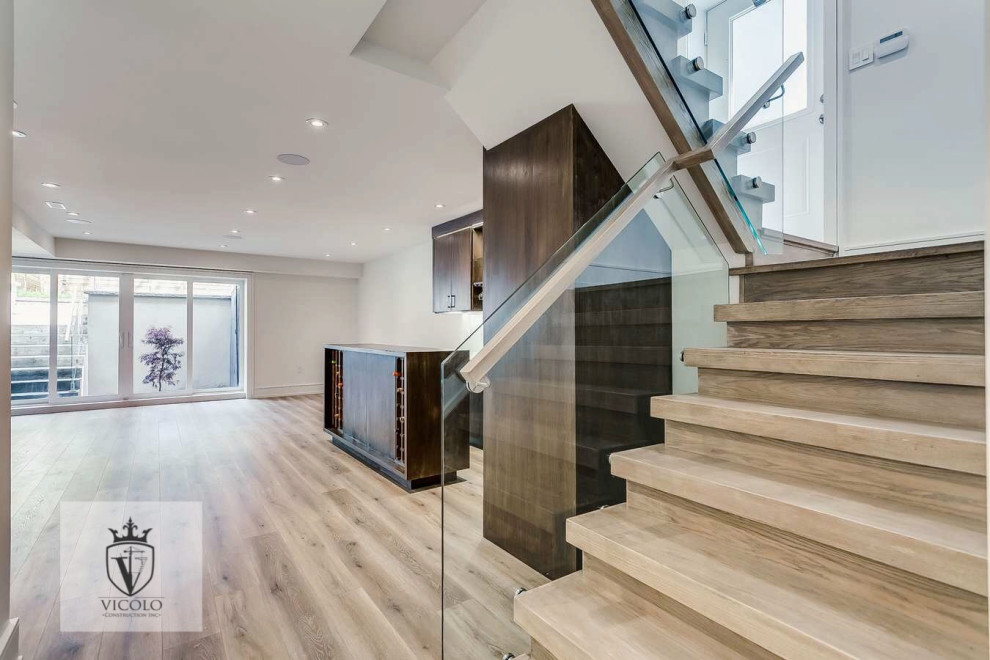 Photo of a mid-sized transitional wood straight staircase with wood risers, glass railing and panelled walls.