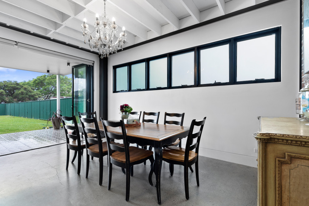 Cette image montre une très grande salle à manger ouverte sur le salon urbaine avec un mur blanc, sol en béton ciré, un sol gris et poutres apparentes.