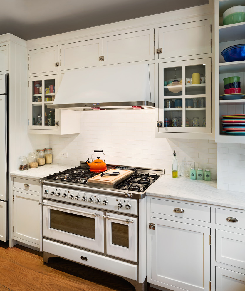 This is an example of a mid-sized traditional l-shaped separate kitchen in New York with shaker cabinets, white cabinets, marble benchtops, white splashback, subway tile splashback, white appliances, medium hardwood floors and with island.