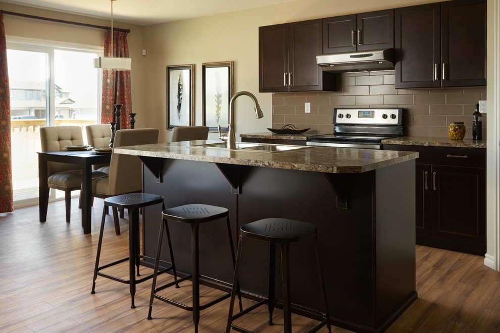 Mid-sized transitional single-wall light wood floor and brown floor eat-in kitchen photo in Edmonton with a double-bowl sink, recessed-panel cabinets, black cabinets, granite countertops, brown backsplash, subway tile backsplash, stainless steel appliances and an island