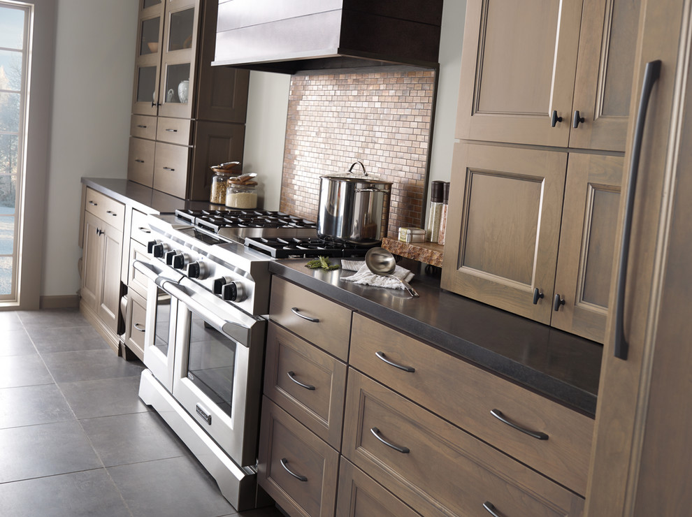 Kitchen - large transitional galley slate floor kitchen idea with an undermount sink, brown cabinets, quartz countertops, beige backsplash, mosaic tile backsplash, stainless steel appliances, an island and recessed-panel cabinets