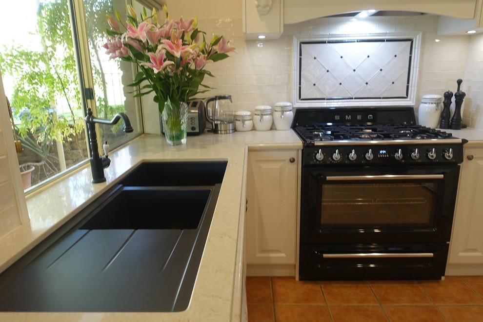Design ideas for a mediterranean u-shaped eat-in kitchen in Melbourne with an undermount sink, subway tile splashback, black appliances, raised-panel cabinets, beige cabinets, granite benchtops, white splashback, terra-cotta floors and a peninsula.