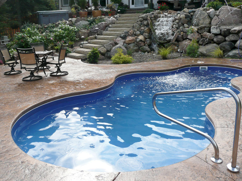 This is an example of a mid-sized contemporary backyard kidney-shaped pool in Chicago with a water feature and concrete slab.