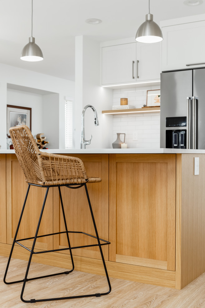 Mid-sized transitional single-wall light wood floor and beige floor eat-in kitchen photo in Vancouver with an undermount sink, shaker cabinets, white cabinets, quartzite countertops, white backsplash, subway tile backsplash, stainless steel appliances, an island and white countertops