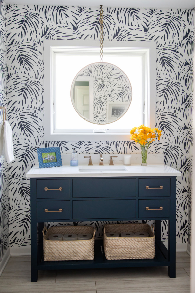 Inspiration for a mid-sized eclectic porcelain tile, brown floor and wallpaper powder room remodel in Milwaukee with flat-panel cabinets, blue cabinets, a two-piece toilet, blue walls, an undermount sink, quartz countertops, white countertops and a freestanding vanity