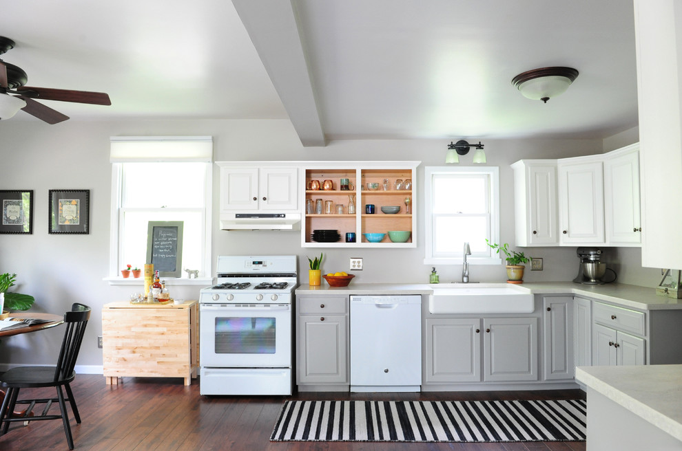Inspiration for a mid-sized transitional l-shaped open plan kitchen in Indianapolis with a farmhouse sink, raised-panel cabinets, white cabinets, solid surface benchtops, white appliances, vinyl floors and no island.