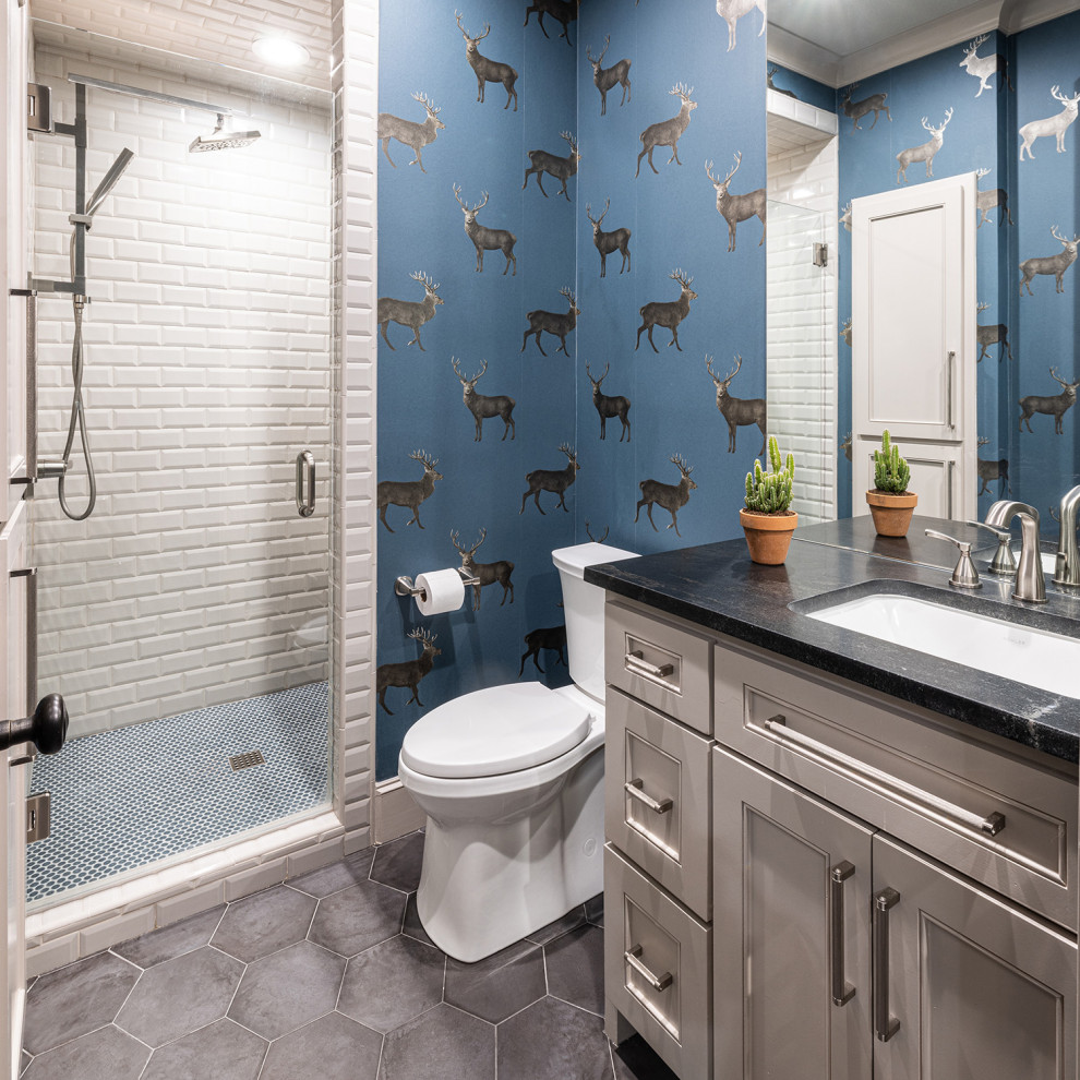 Photo of a mid-sized transitional 3/4 bathroom in Dallas with recessed-panel cabinets, beige cabinets, an alcove shower, a one-piece toilet, white tile, ceramic tile, blue walls, porcelain floors, an undermount sink, engineered quartz benchtops, grey floor, a hinged shower door, black benchtops, a single vanity, a built-in vanity and wallpaper.