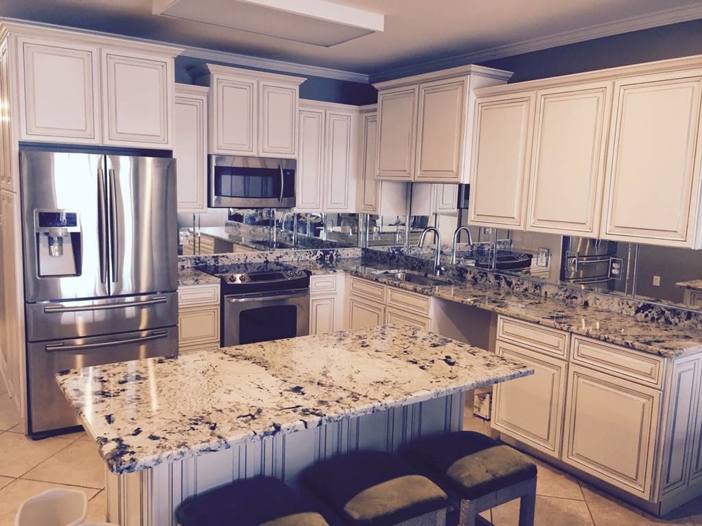 Example of a mid-sized transitional l-shaped ceramic tile and beige floor eat-in kitchen design with an undermount sink, raised-panel cabinets, distressed cabinets, granite countertops, metallic backsplash, mirror backsplash, stainless steel appliances and an island