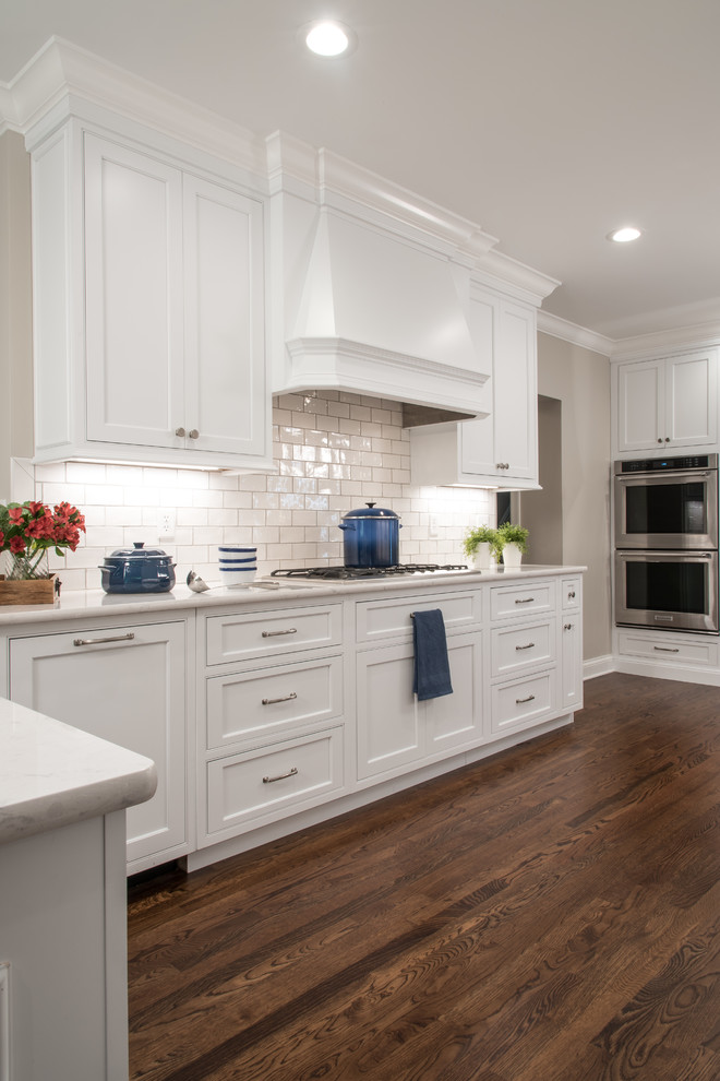 Photo of a large traditional single-wall kitchen in St Louis with an undermount sink, dark hardwood floors, brown floor, recessed-panel cabinets, white cabinets, onyx benchtops, white splashback, subway tile splashback, stainless steel appliances, white benchtop and a peninsula.