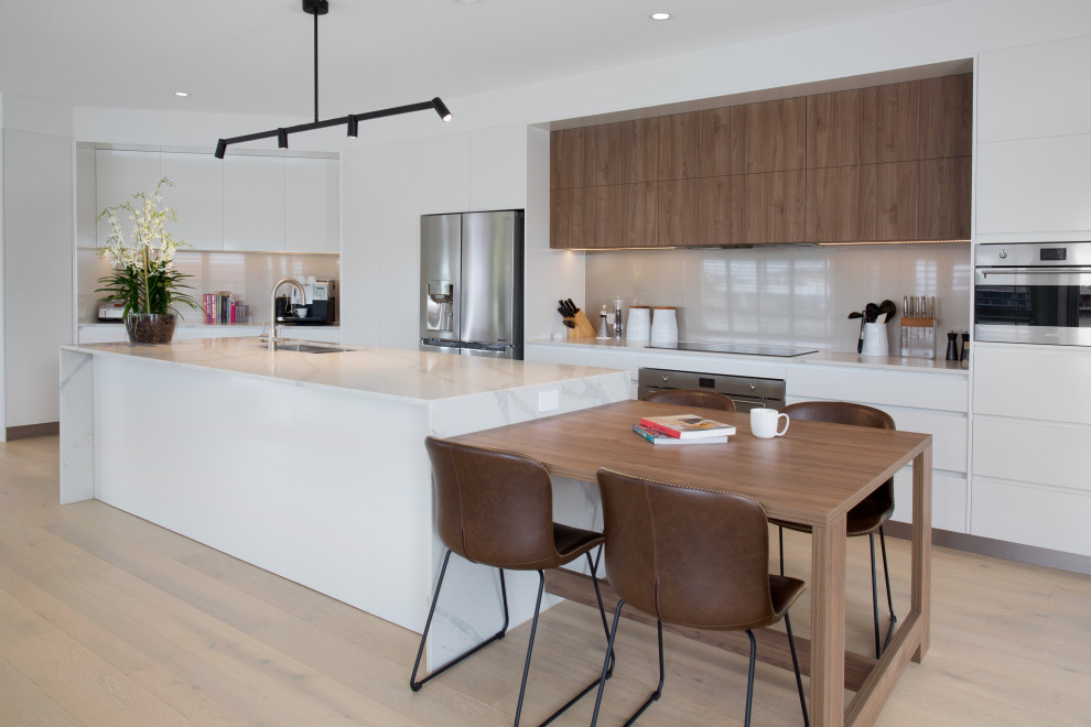Inspiration for a large contemporary galley eat-in kitchen in Gold Coast - Tweed with an undermount sink, quartz benchtops, glass sheet splashback, stainless steel appliances, light hardwood floors, with island, brown floor, white benchtop, flat-panel cabinets, white cabinets and beige splashback.