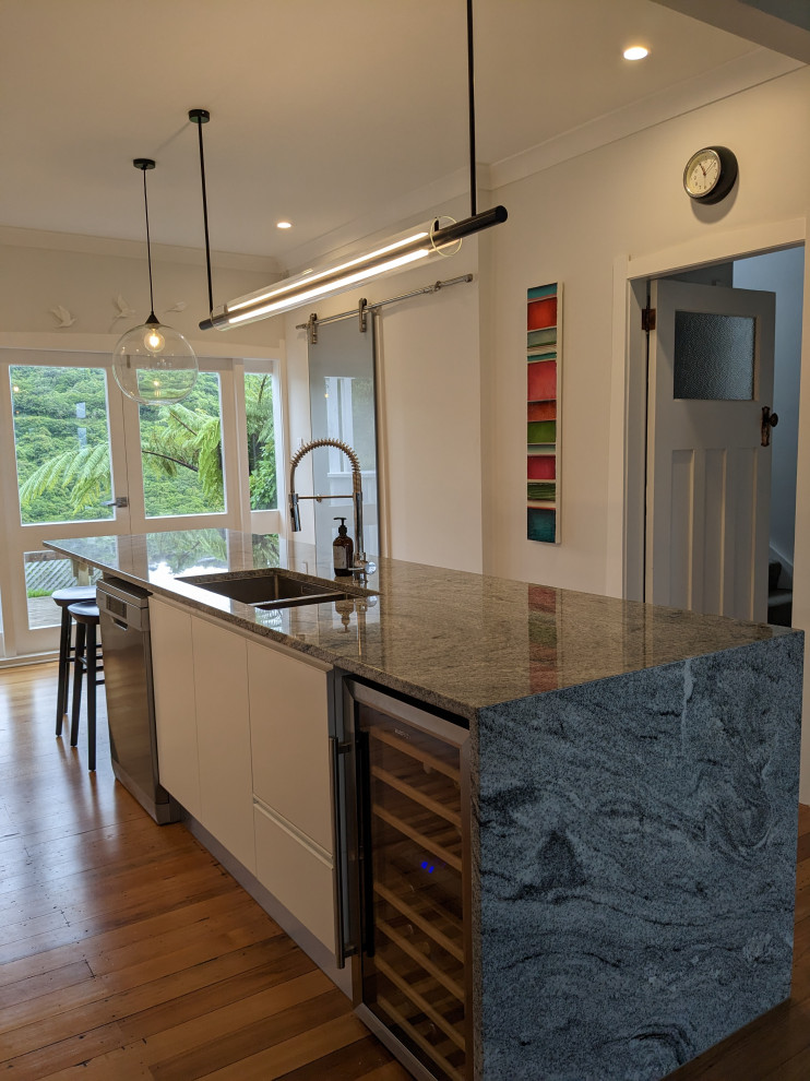Diseño de cocina contemporánea de tamaño medio con puertas de armario blancas, encimera de granito, electrodomésticos de acero inoxidable, suelo de madera en tonos medios, una isla y encimeras grises