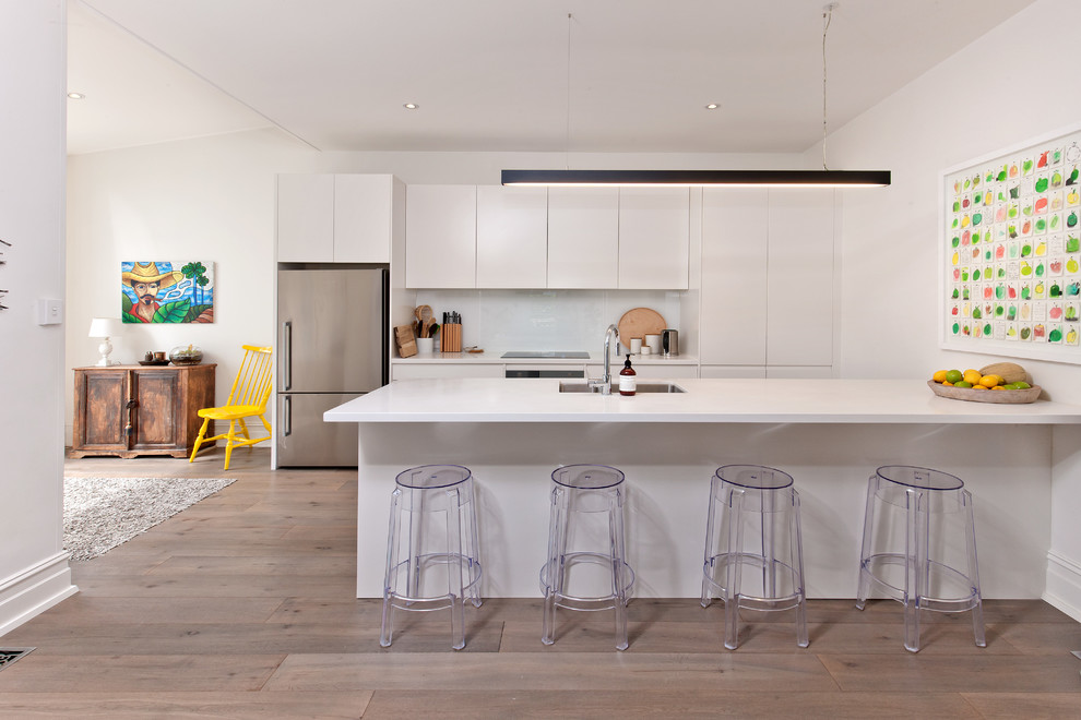 Inspiration for a mid-sized scandinavian single-wall eat-in kitchen in Other with a double-bowl sink, flat-panel cabinets, white cabinets, quartz benchtops, white splashback, glass sheet splashback, stainless steel appliances, laminate floors, with island, grey floor and white benchtop.