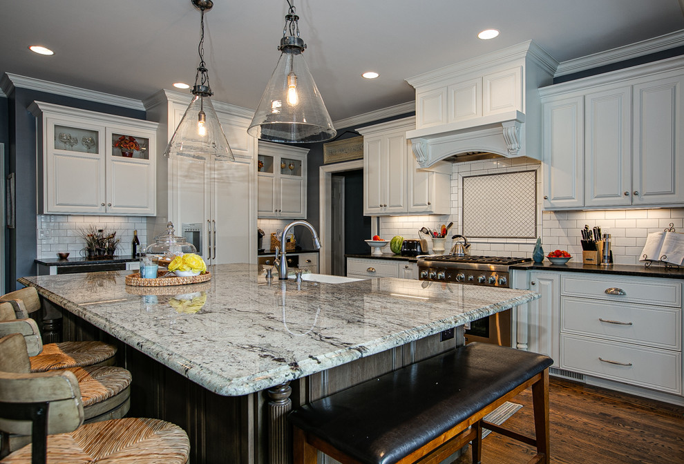 Example of a large transitional l-shaped brown floor and medium tone wood floor open concept kitchen design in Charlotte with white cabinets, granite countertops, white backsplash, stainless steel appliances, an island, raised-panel cabinets, porcelain backsplash, a farmhouse sink and white countertops