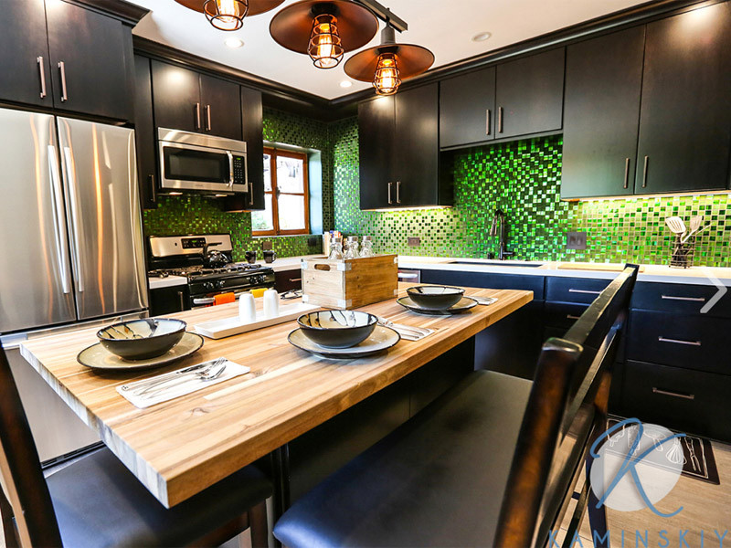 На фото: угловая кухня среднего размера в стиле неоклассика (современная классика) с обеденным столом, накладной мойкой, плоскими фасадами, зеленым фартуком, фартуком из стеклянной плитки, полом из фанеры, островом и коричневым полом с