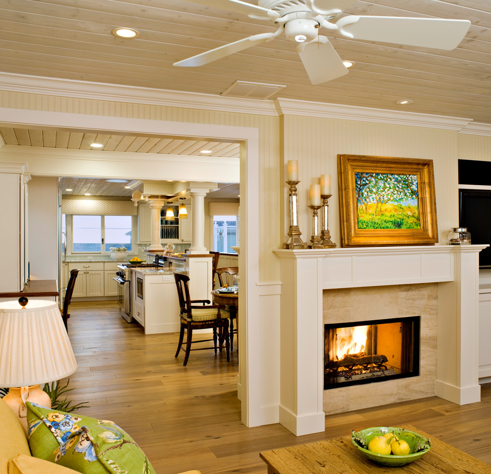 This is an example of a mid-sized beach style open concept living room in Los Angeles with yellow walls, light hardwood floors, a two-sided fireplace, a stone fireplace surround and a wall-mounted tv.