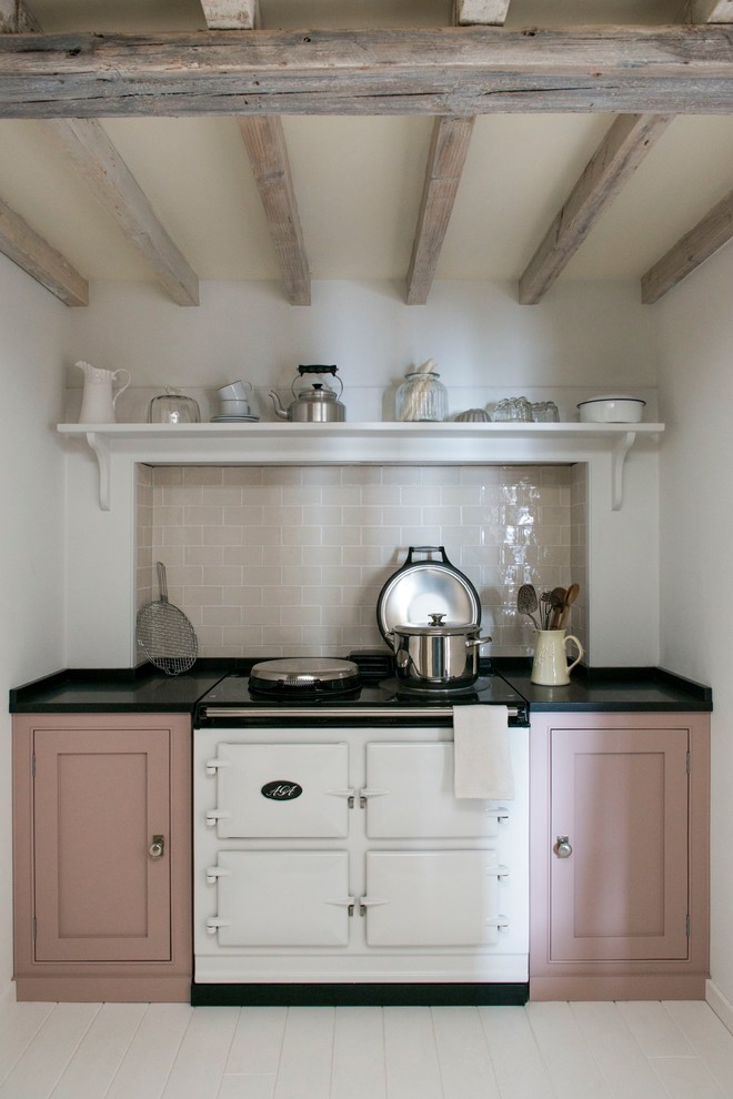 This is an example of a country kitchen in London with shaker cabinets, white appliances, painted wood floors and no island.