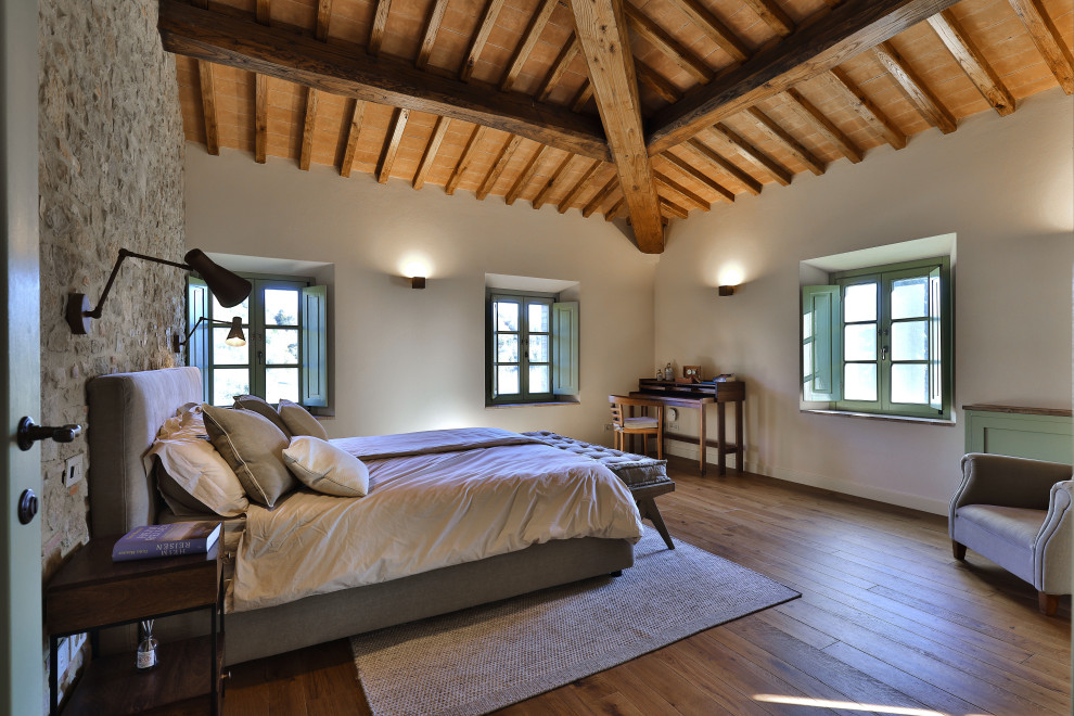 Großes Landhaus Hauptschlafzimmer mit gelber Wandfarbe, gebeiztem Holzboden, braunem Boden und freigelegten Dachbalken in Florenz