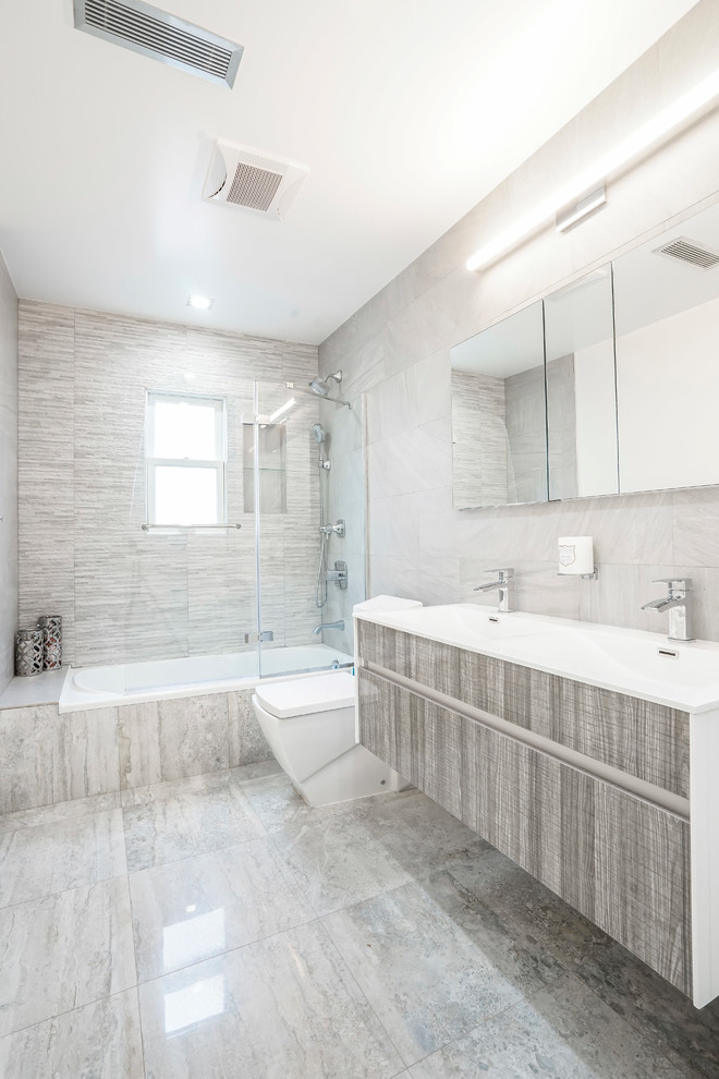 This is an example of a large contemporary kids bathroom in New York with flat-panel cabinets, grey cabinets, a drop-in tub, an alcove shower, a one-piece toilet, gray tile, porcelain tile, grey walls, ceramic floors, a drop-in sink, onyx benchtops, grey floor, a hinged shower door and white benchtops.