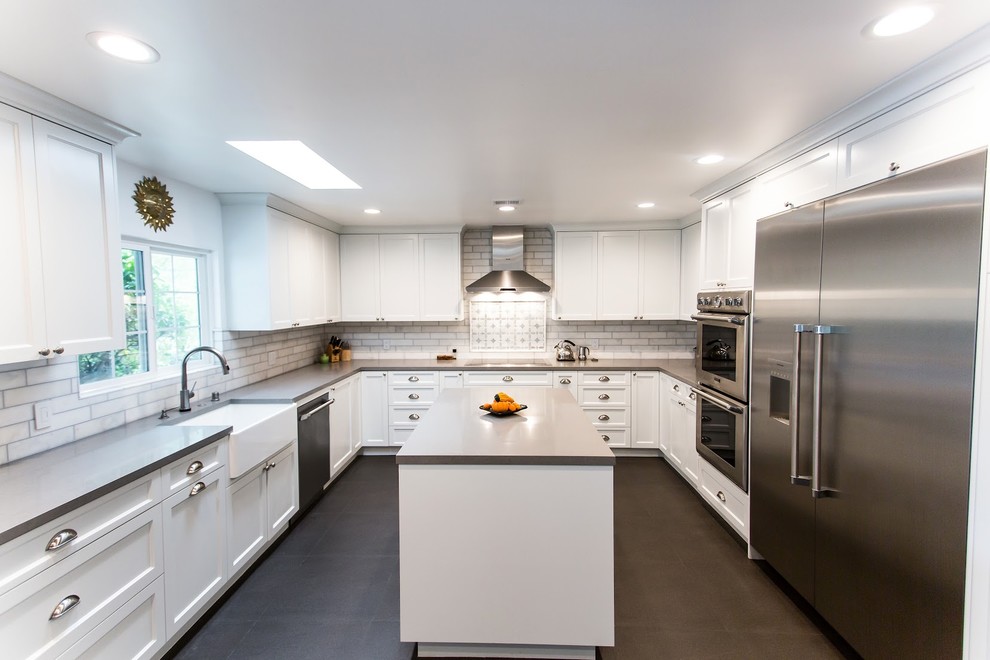 Inspiration for an expansive modern u-shaped eat-in kitchen in Los Angeles with a farmhouse sink, shaker cabinets, white cabinets, granite benchtops, white splashback, subway tile splashback, stainless steel appliances, ceramic floors, with island, grey floor and grey benchtop.