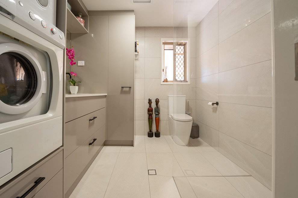 This is an example of a mid-sized contemporary utility room in Brisbane with quartz benchtops, porcelain floors, a stacked washer and dryer and beige floor.