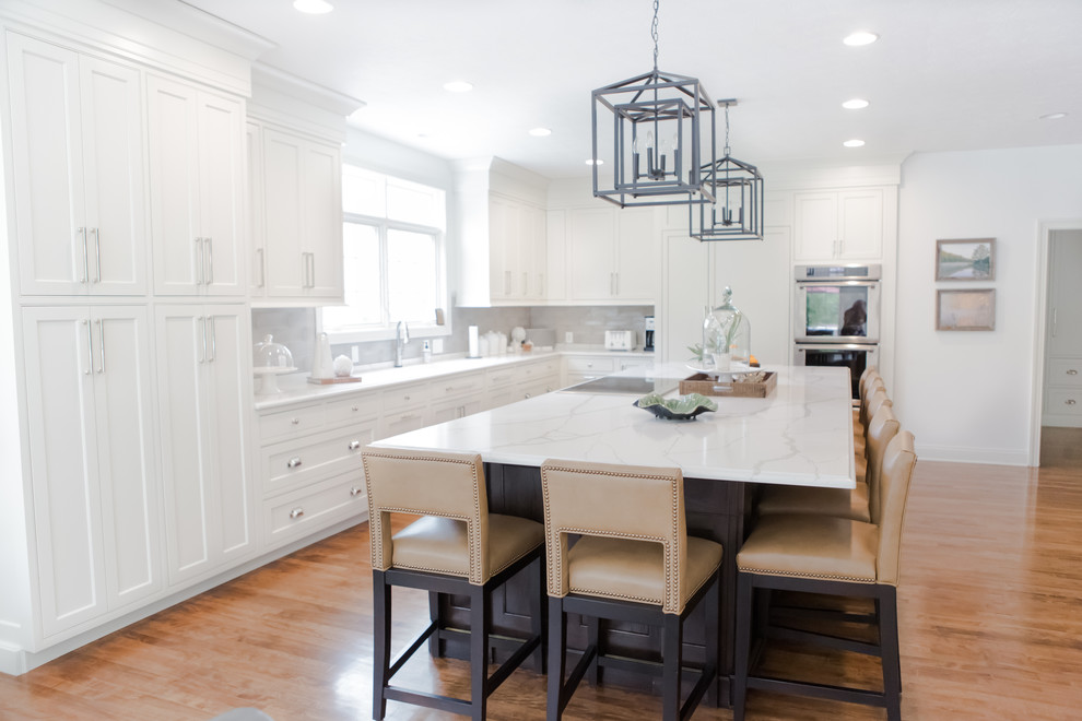 Design ideas for a large arts and crafts galley open plan kitchen in Indianapolis with an undermount sink, shaker cabinets, white cabinets, quartzite benchtops, grey splashback, subway tile splashback, panelled appliances, medium hardwood floors, with island and brown floor.