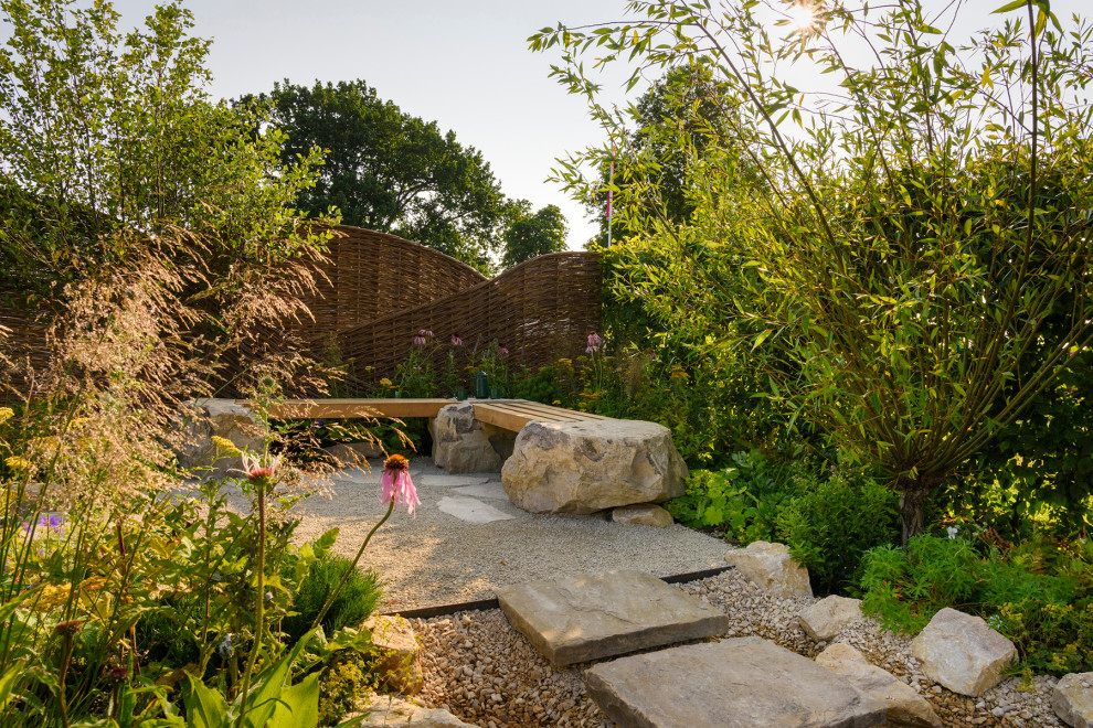 Foto di un giardino xeriscape minimal esposto in pieno sole dietro casa con sassi di fiume e recinzione in legno