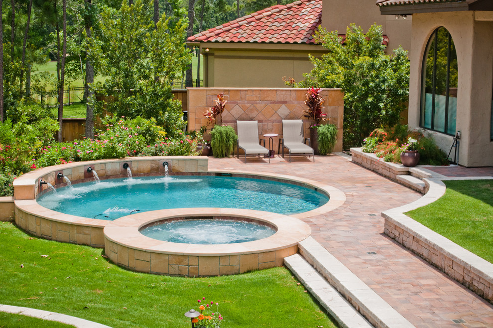 This is an example of a mid-sized traditional backyard round pool in Houston with a hot tub and natural stone pavers.