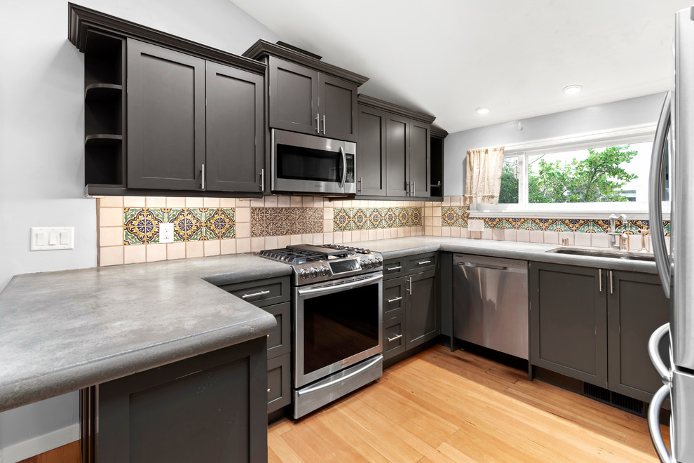 Photo of a small traditional u-shaped kitchen in San Francisco with an undermount sink, shaker cabinets, distressed cabinets, concrete benchtops, ceramic splashback, stainless steel appliances, medium hardwood floors, brown floor and grey benchtop.
