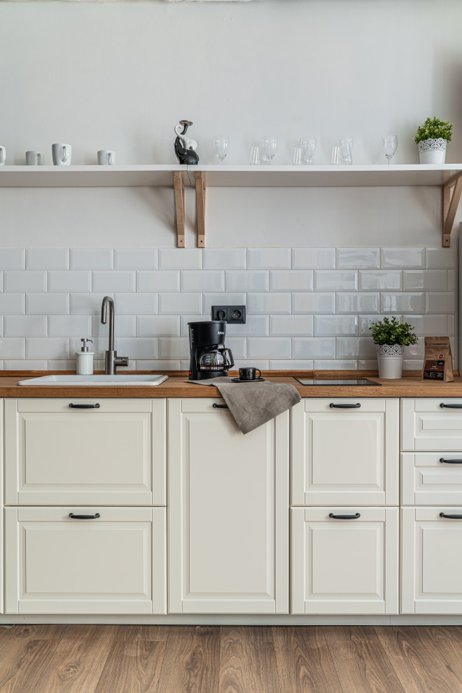 Bild på ett mellanstort nordiskt brun linjärt brunt kök med öppen planlösning, med en enkel diskho, släta luckor, vita skåp, träbänkskiva, vitt stänkskydd, stänkskydd i tegel, vita vitvaror, laminatgolv och beiget golv