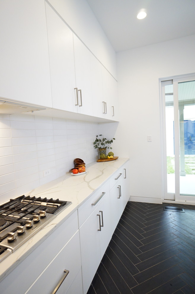 This is an example of a small modern l-shaped separate kitchen in Richmond with an undermount sink, flat-panel cabinets, white cabinets, quartz benchtops, white splashback, ceramic splashback, stainless steel appliances, ceramic floors, with island, black floor and white benchtop.