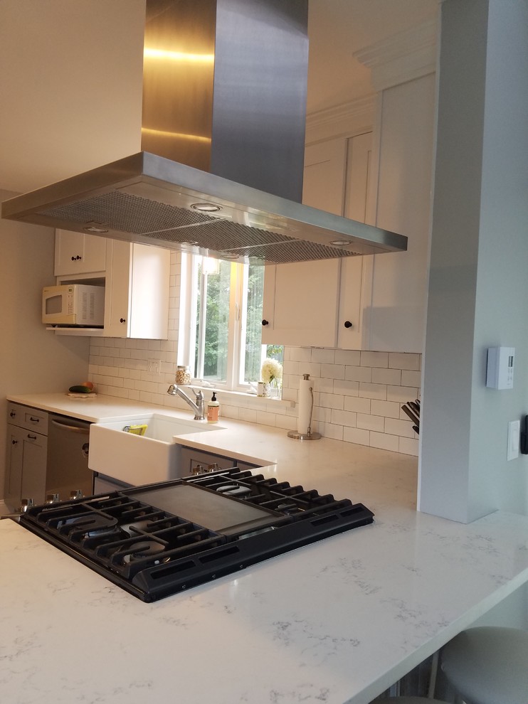 Kitchen - small transitional kitchen idea in Providence with a farmhouse sink, shaker cabinets, white cabinets, marble countertops, white backsplash, subway tile backsplash, stainless steel appliances, a peninsula and white countertops