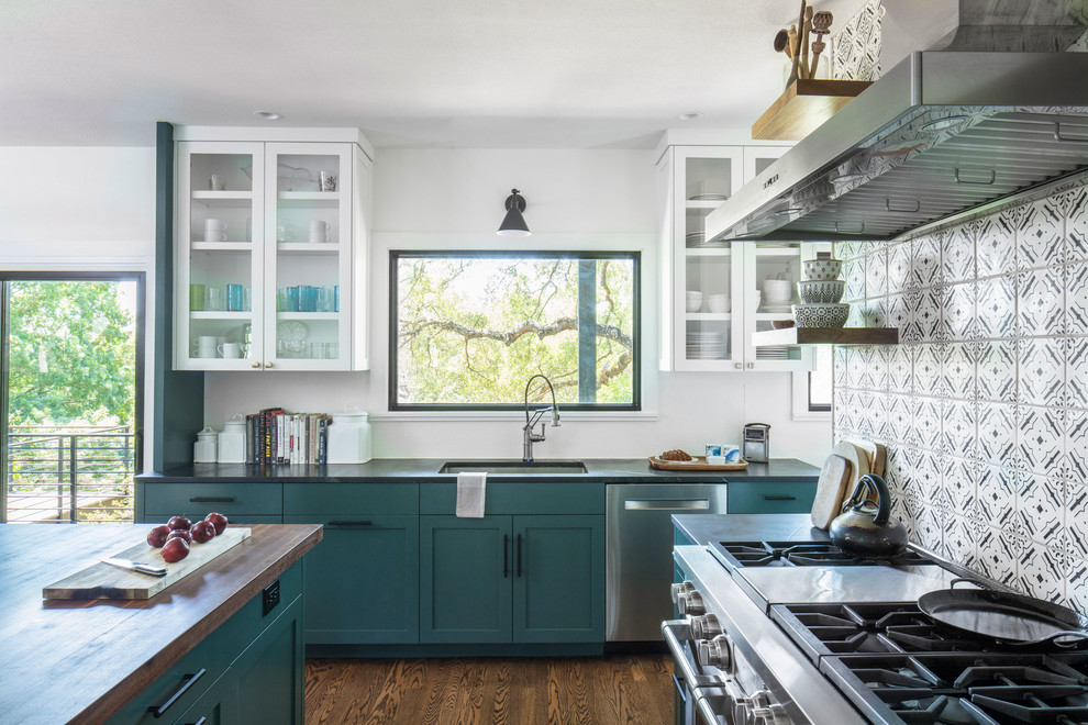 Design ideas for a mid-sized traditional kitchen in Austin with an undermount sink, glass-front cabinets, white cabinets, soapstone benchtops, white splashback, stainless steel appliances, medium hardwood floors, with island, brown floor and black benchtop.