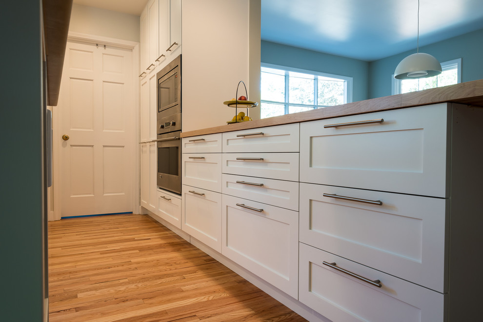 Inspiration for an arts and crafts galley eat-in kitchen in Seattle with recessed-panel cabinets, white cabinets, wood benchtops, light hardwood floors and no island.