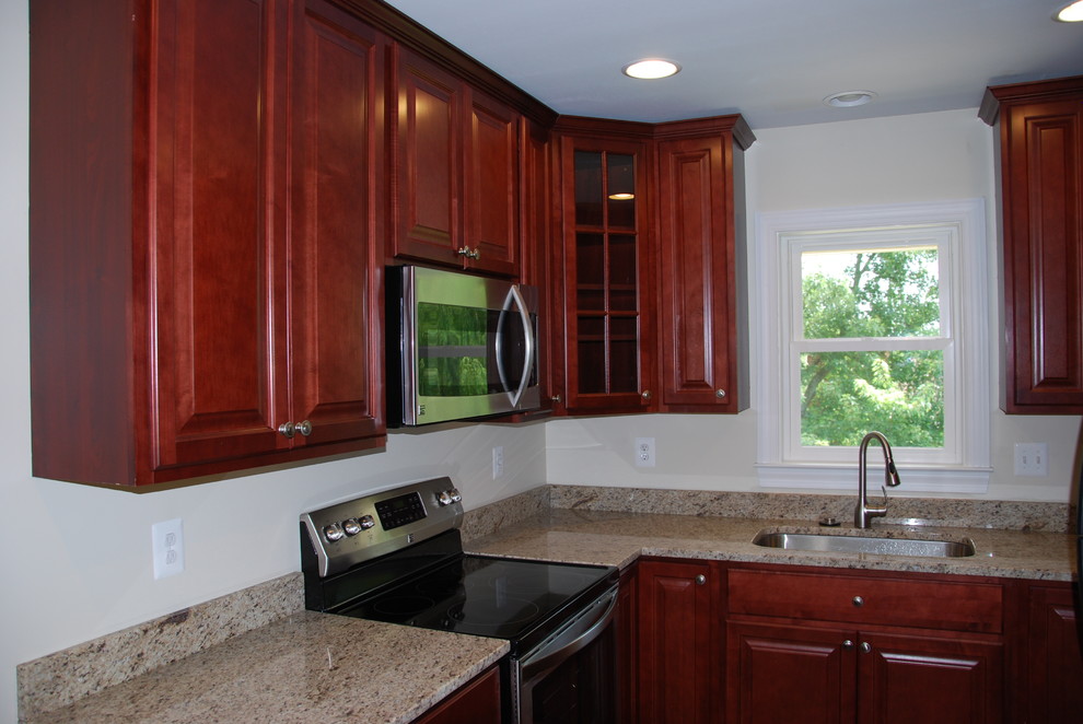 Mid-sized traditional u-shaped separate kitchen in DC Metro with an undermount sink, raised-panel cabinets, dark wood cabinets, granite benchtops, stainless steel appliances, dark hardwood floors, no island, brown floor and beige benchtop.