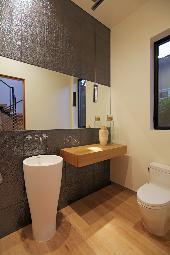 Contemporary powder room in Los Angeles with a pedestal sink, wood benchtops, a one-piece toilet, gray tile and brown benchtops.