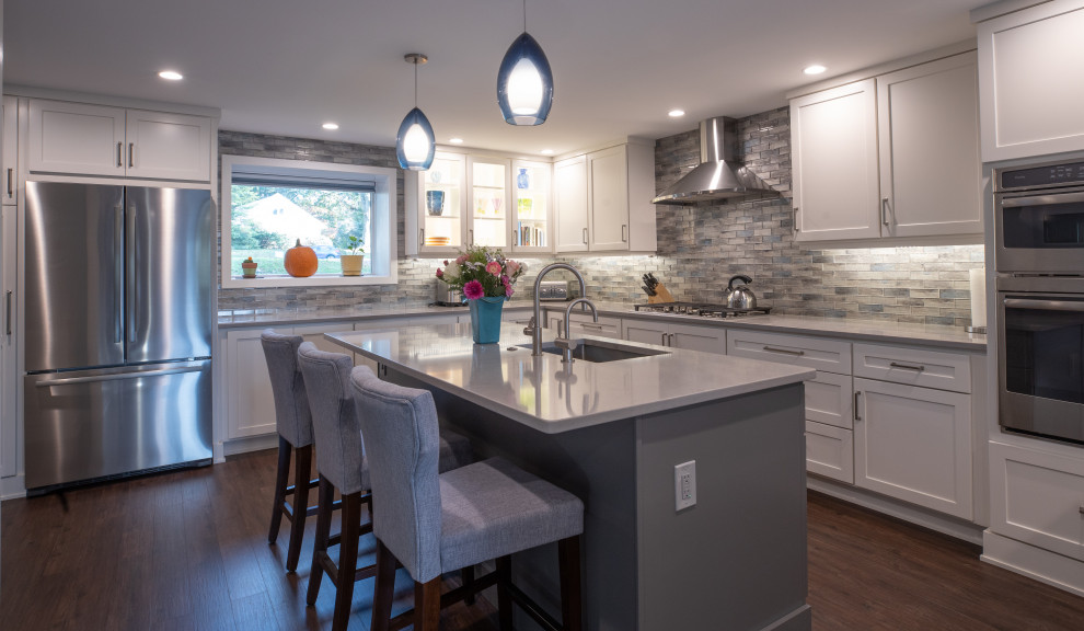 Transitional open plan kitchen in Philadelphia with an undermount sink, shaker cabinets, white cabinets, quartz benchtops, multi-coloured splashback, stainless steel appliances, medium hardwood floors, with island and grey benchtop.