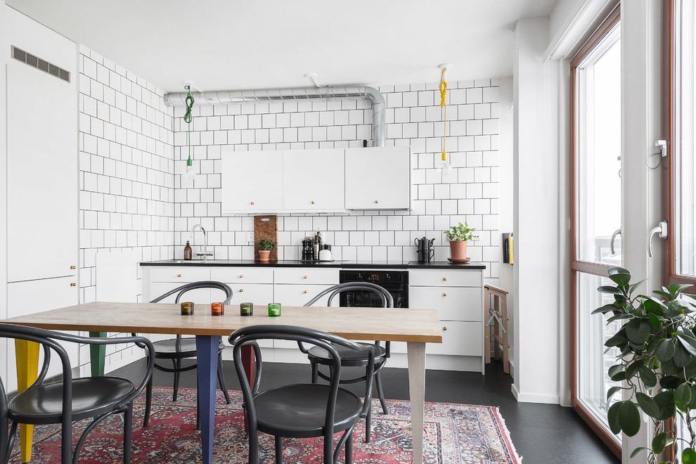 This is an example of a scandinavian l-shaped eat-in kitchen in Stockholm with a drop-in sink, flat-panel cabinets, white splashback, black appliances, no island, black floor and black benchtop.