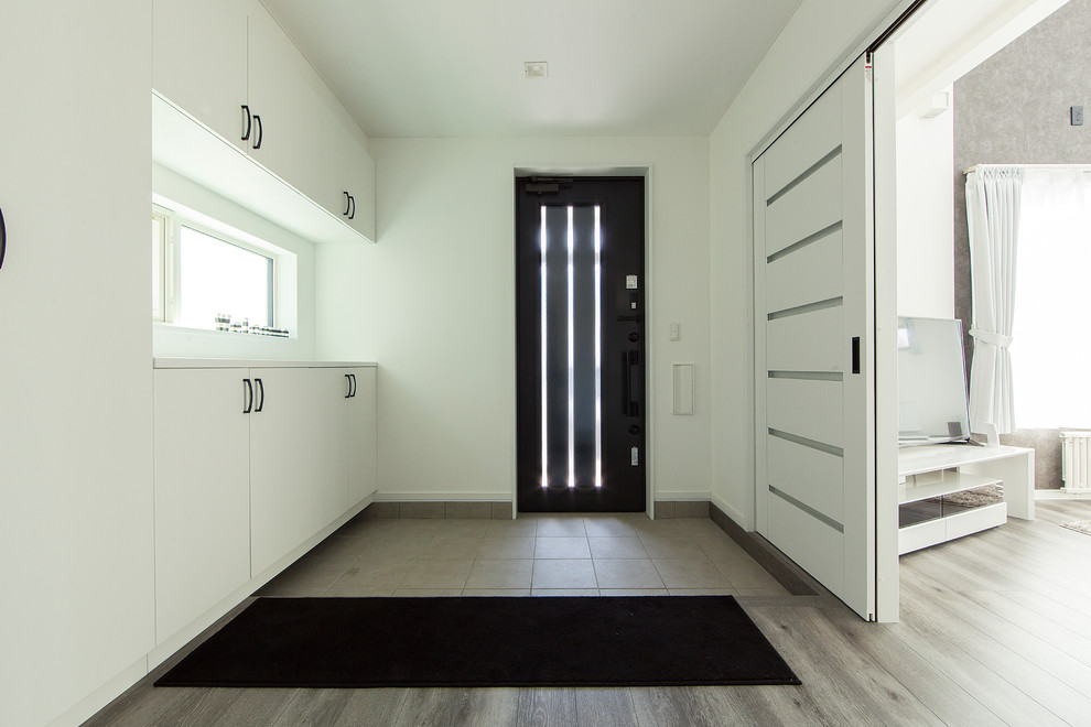 Photo of a contemporary entry hall in Other with white walls, a single front door, a black front door and grey floor.