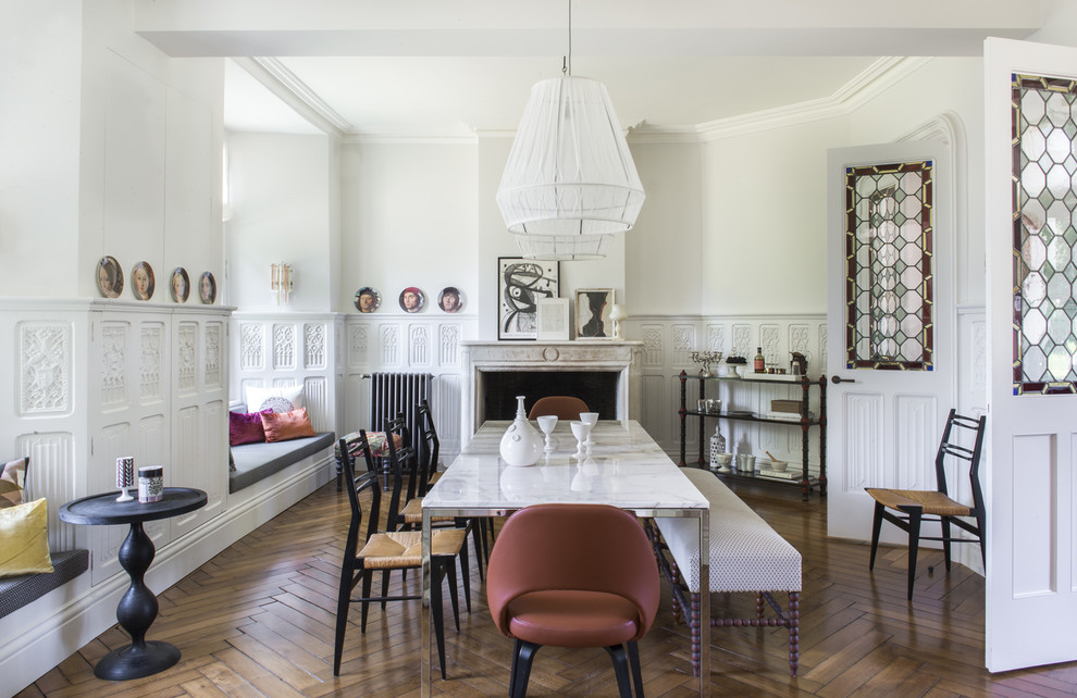 This is an example of an expansive eclectic separate dining room in Paris with white walls, medium hardwood floors, a standard fireplace and a stone fireplace surround.