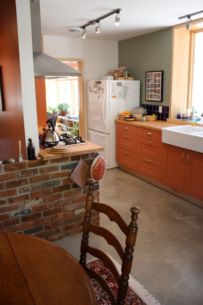 This is an example of a mid-sized transitional galley eat-in kitchen in Toronto with a farmhouse sink, recessed-panel cabinets, orange cabinets, wood benchtops, blue splashback, black appliances, concrete floors and no island.