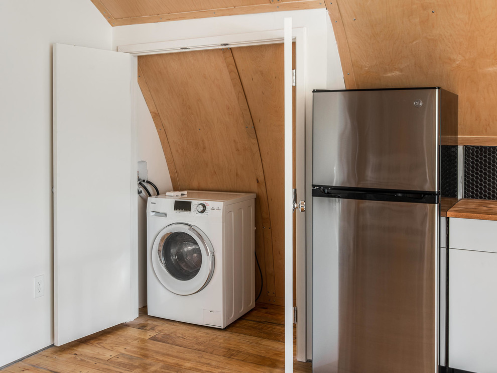 This is an example of a small industrial l-shaped laundry room in Nashville with a drop-in sink, flat-panel cabinets, white cabinets, wood benchtops and light hardwood floors.